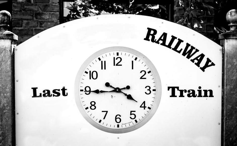 A large, round railway clock mounted on a white signboard with the words 'Last', 'Railway', and 'Train' in bold black letters arranged around the clock face, which displays the time as approximately 3
